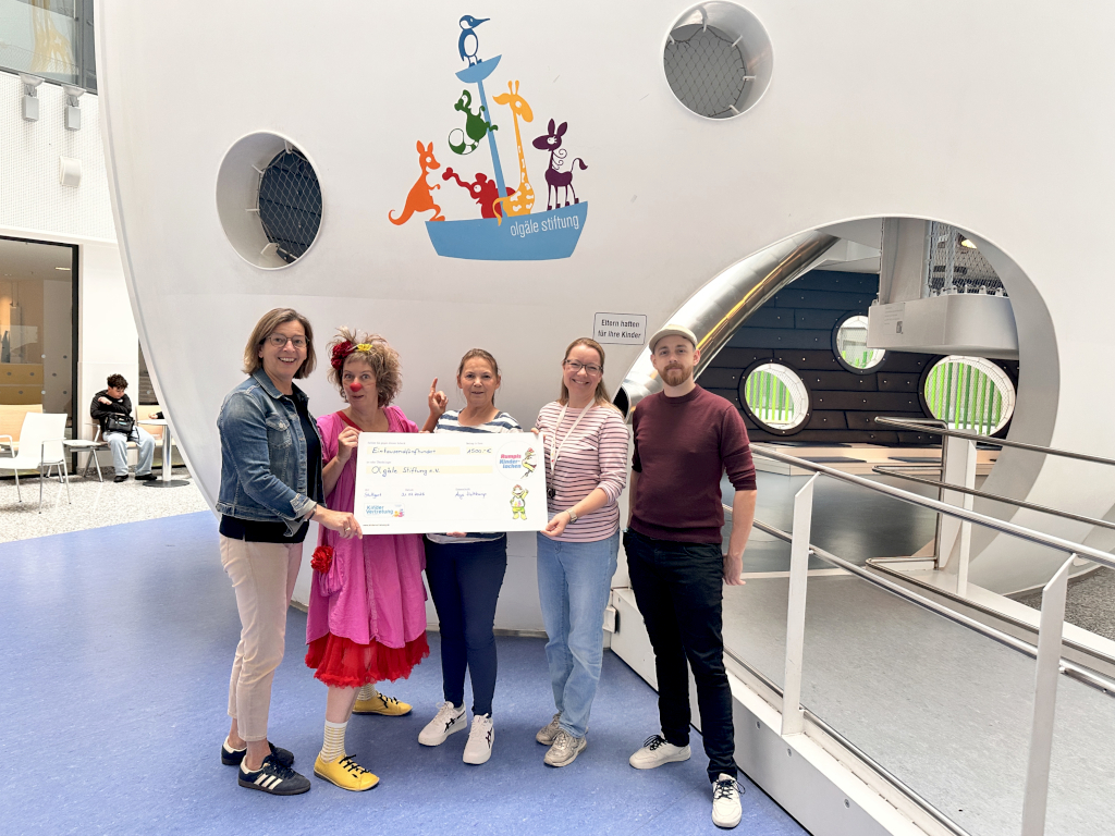 2 Vertreter der Deutschen Kinderhilfe übergeben einen Spendenscheck an 2 Mitarbeiterinnen der Olgäle-Stiftung und einen Klinikclown