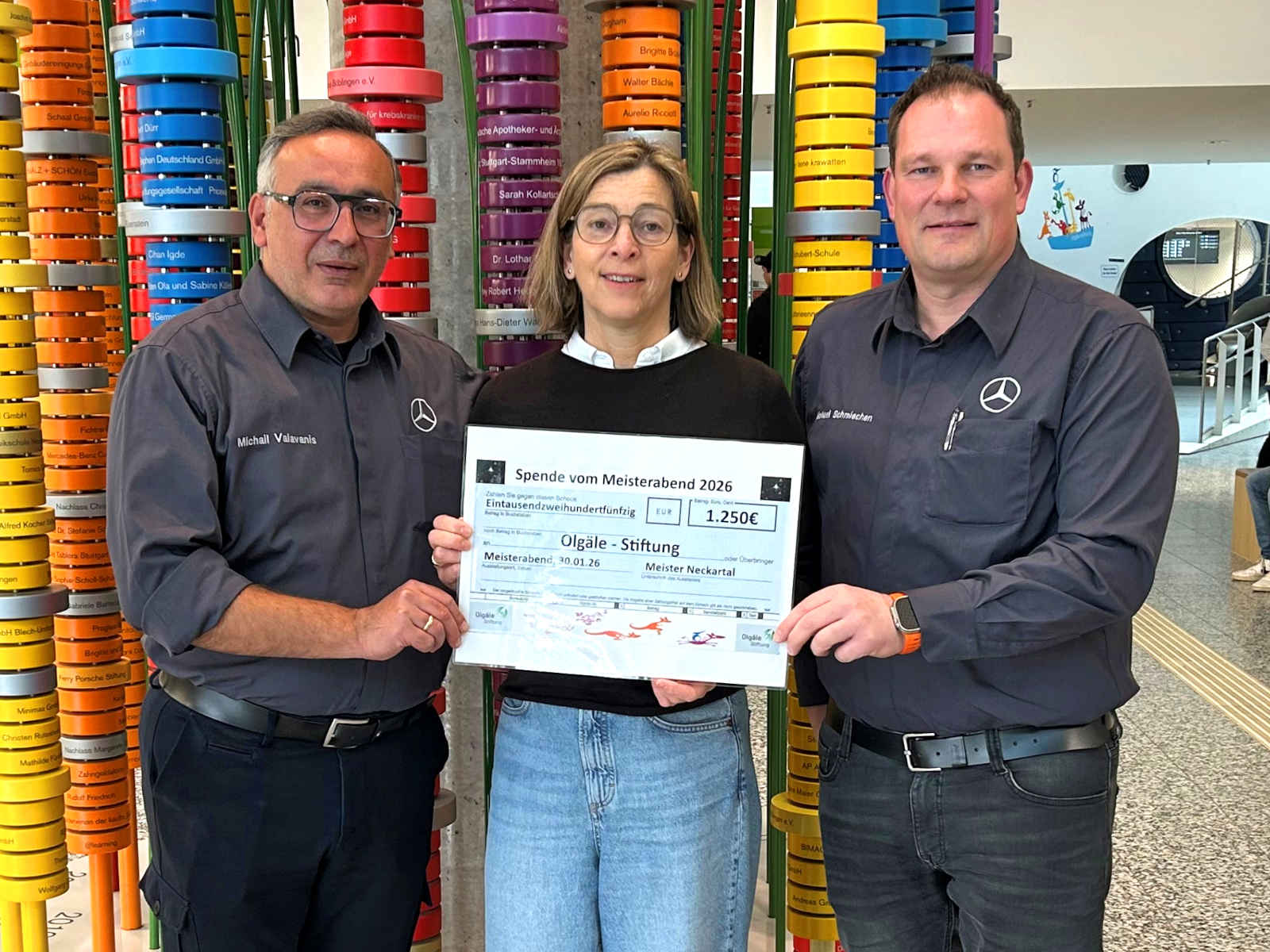 Michail Valavanis und Michael Schmiechen mit Felicitas von Hülsen von der Olgäle-Stiftung halten den symbolischen Spendenscheck