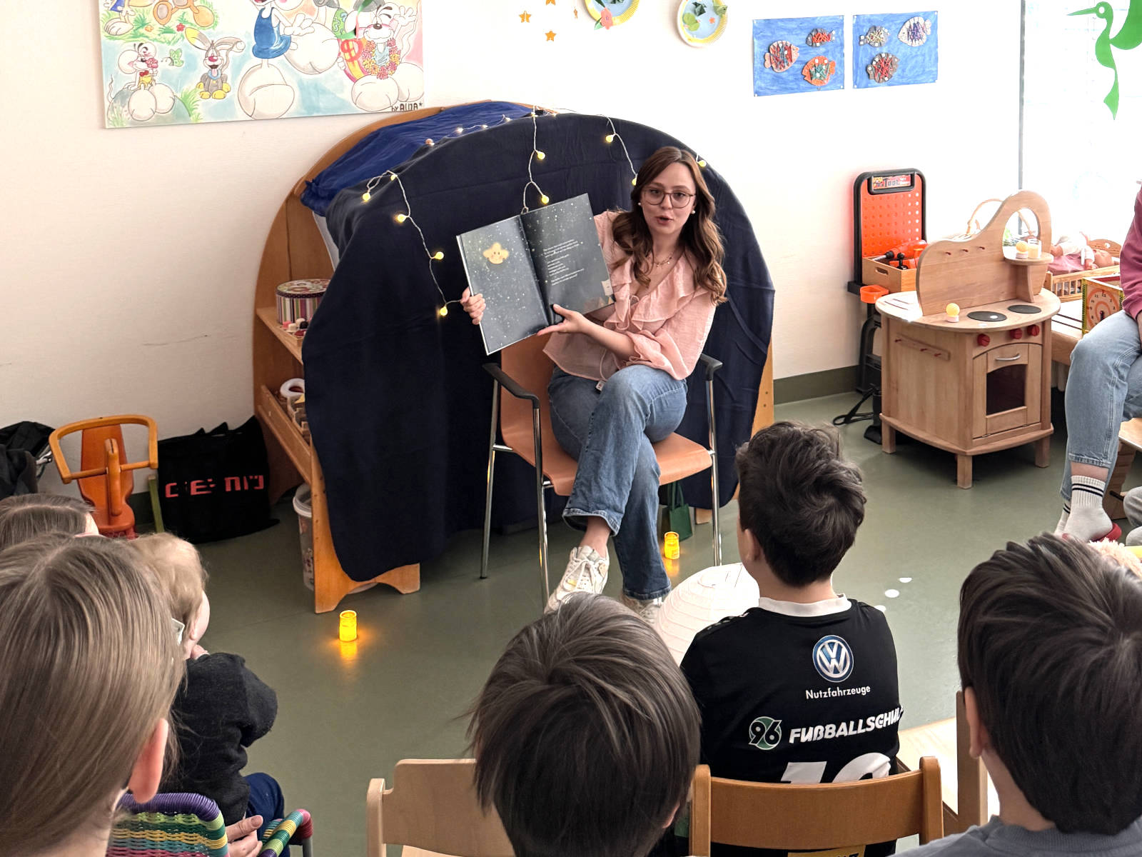 Emilia Melcher sitzt im Spielzimmer von Kindern und liest aus ihrem Buch vor