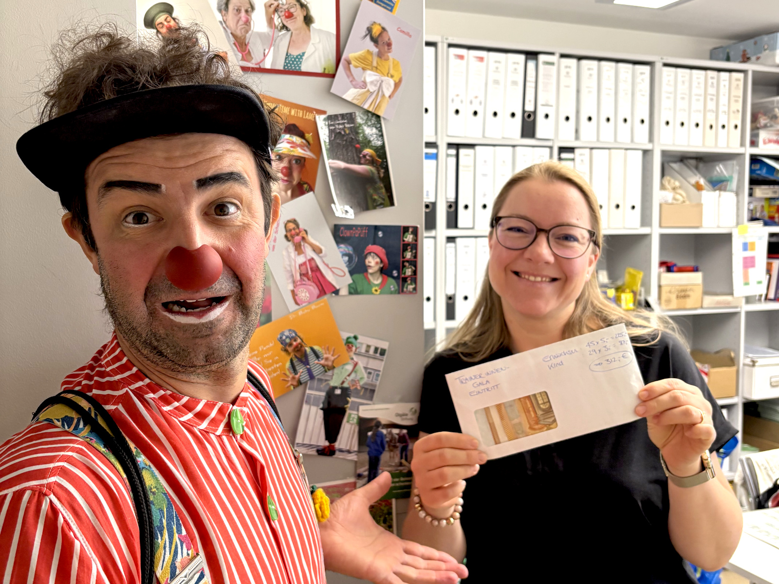 Klinikclown Ghilly Rodriguez mit Anina Sieglin, die den Spenden-Umschlag in den Händen hält, im Büro der Olgäle-Stiftung